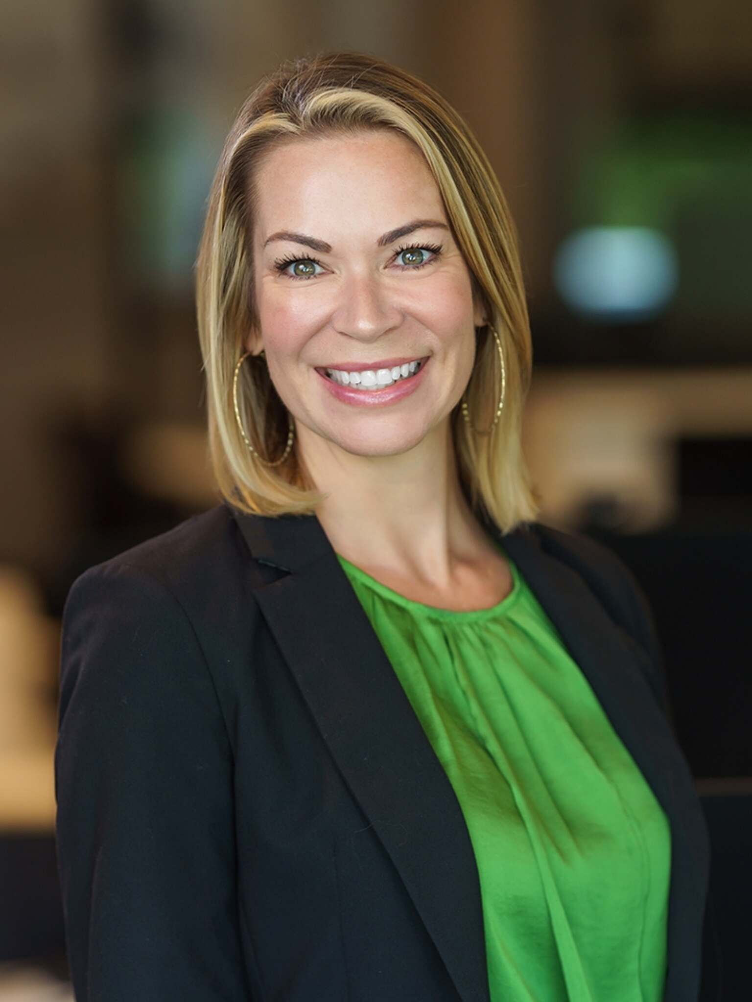 blonde woman smiling for headshot wearing a green top and black blazer