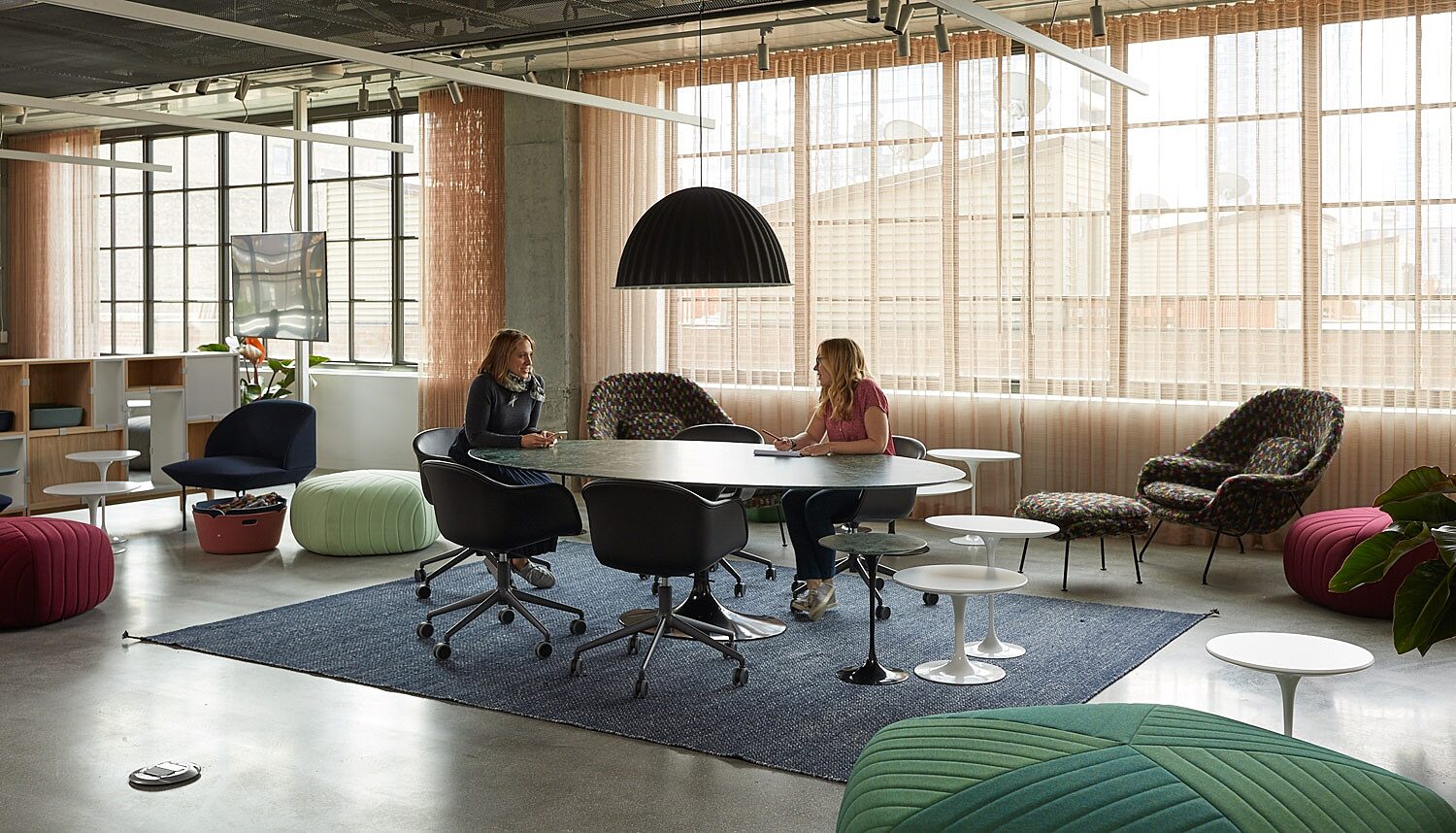 Modern office with collaborative oval table, 5 black chairs, and seating poufs