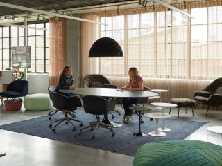 Modern office with collaborative oval table, 5 black chairs, and seating poufs