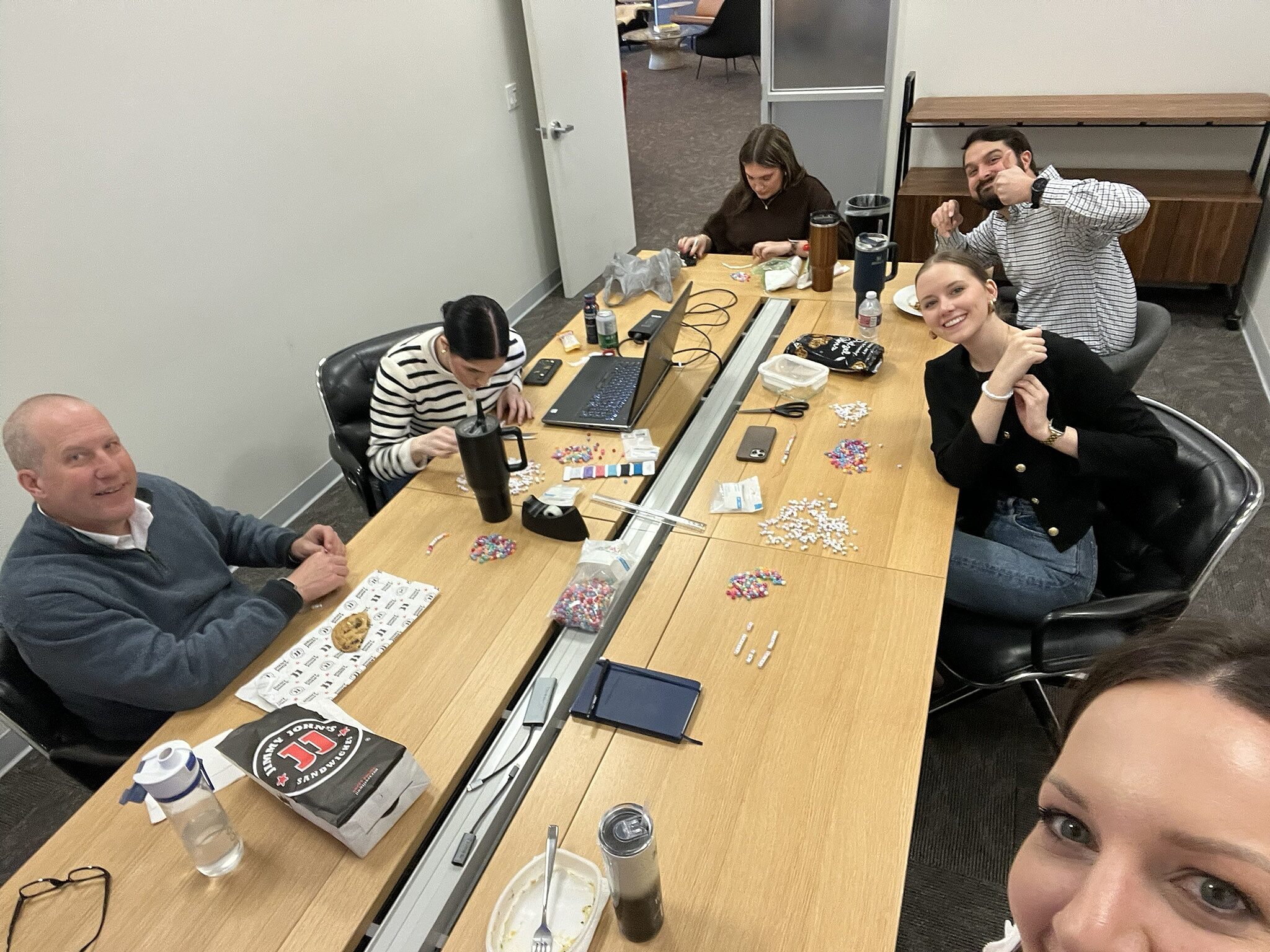 a group of people sitting at a conference table making friendship bracelets
