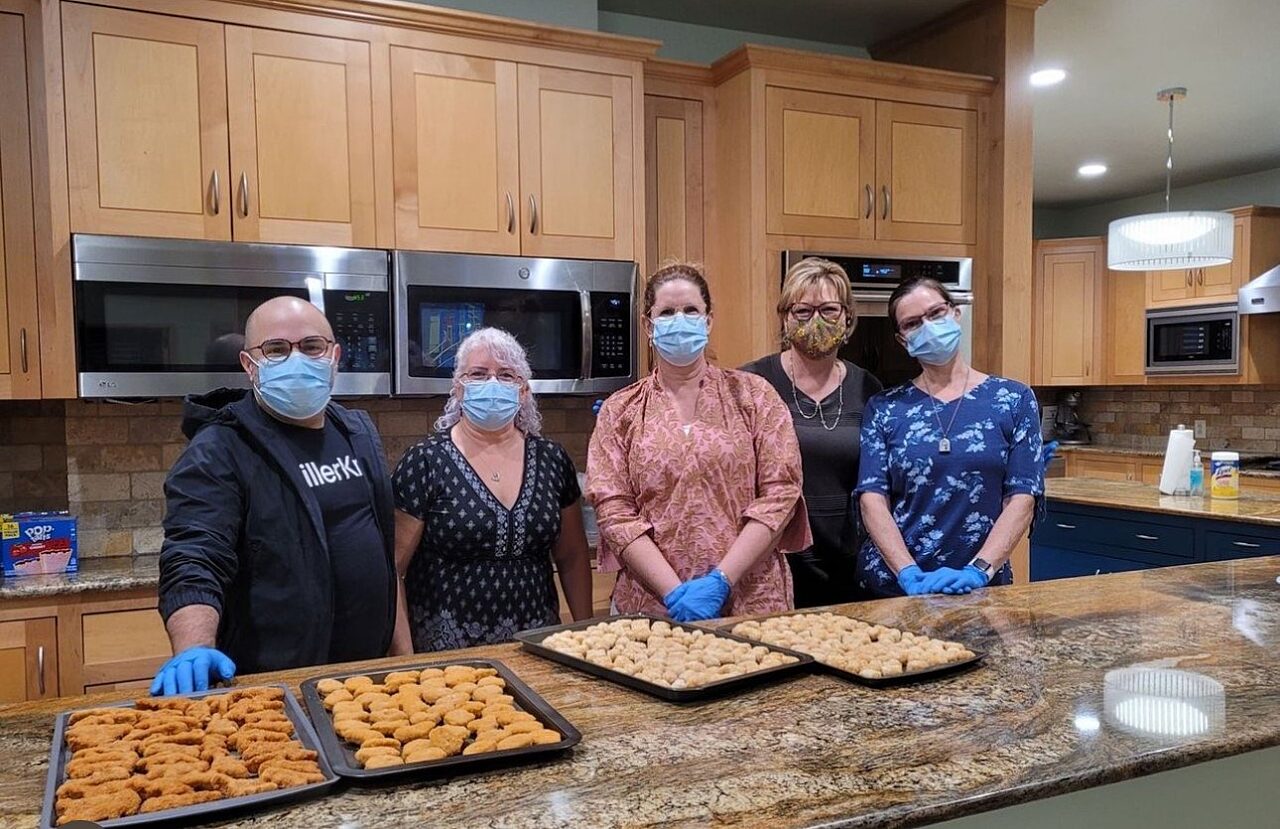 A group of people standing in front of prepped meals to serve at RMHFW