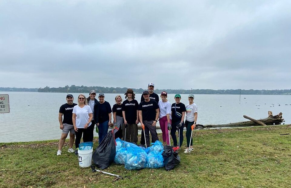 picture of a group of people standing in front of a lake with bags full of trash