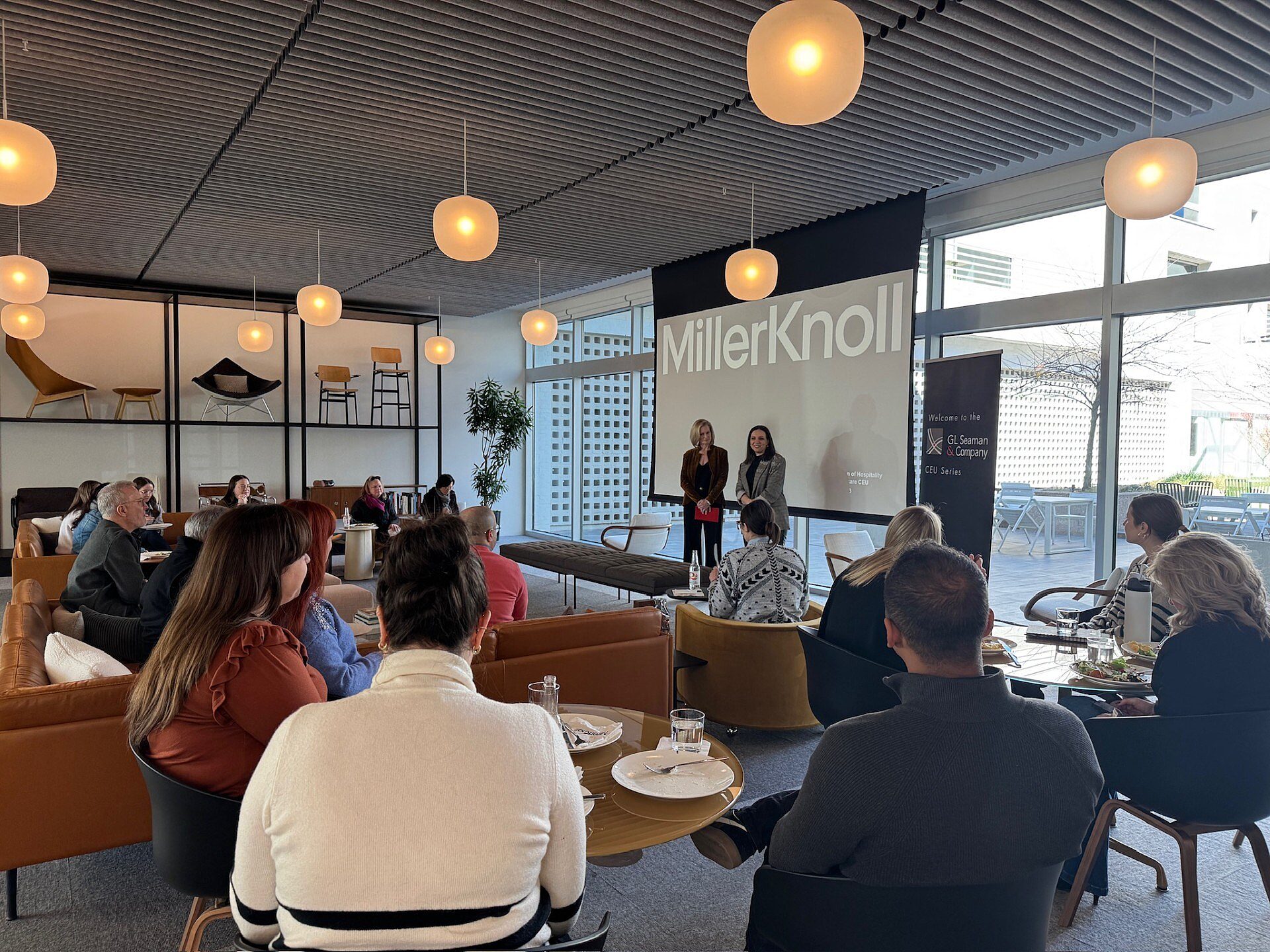 Two women speaking at a CEU event with audience members sitting down in chairs listening