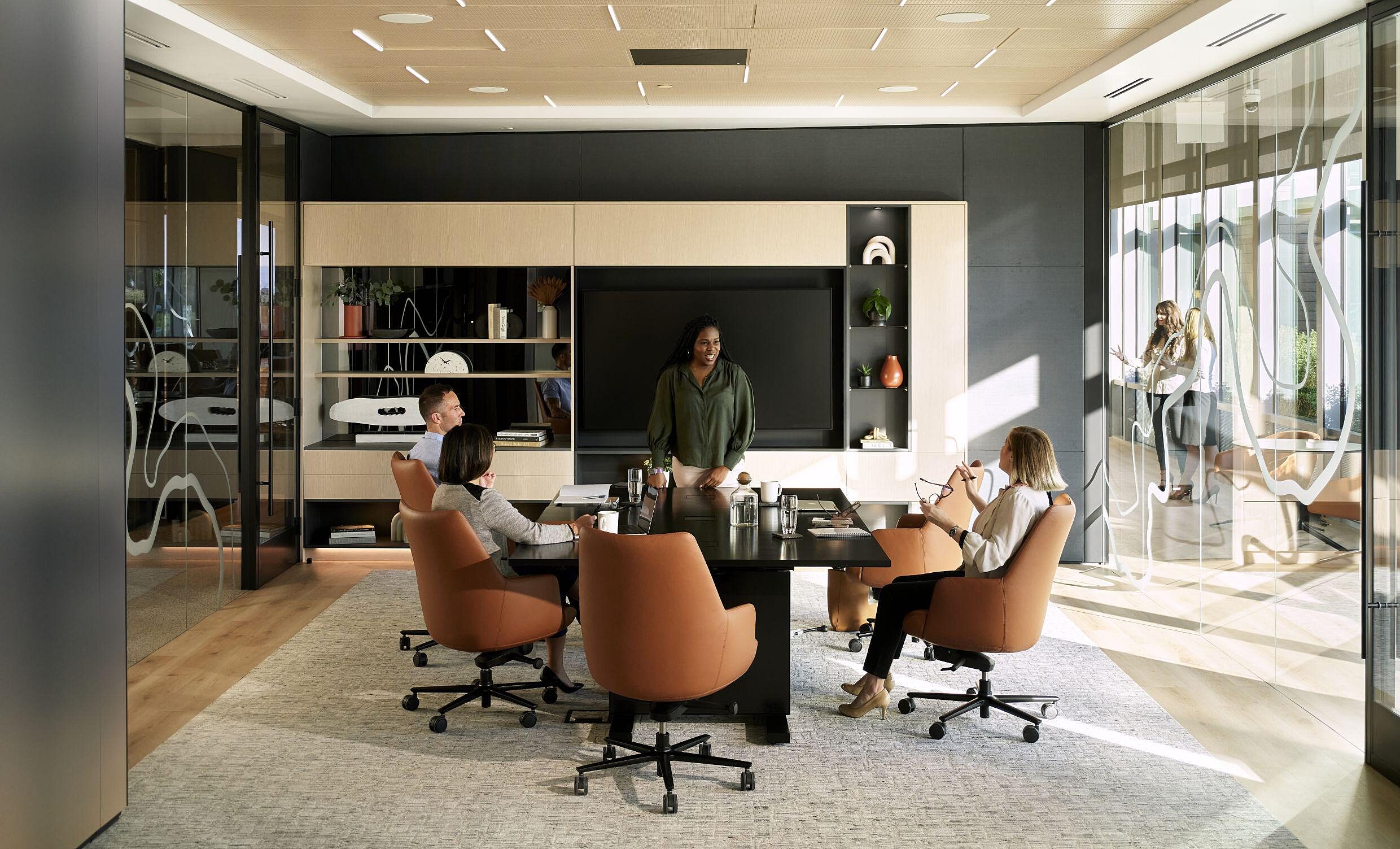 coworkers having a meeting in a conference room sitting at a black table in brown leather chairs