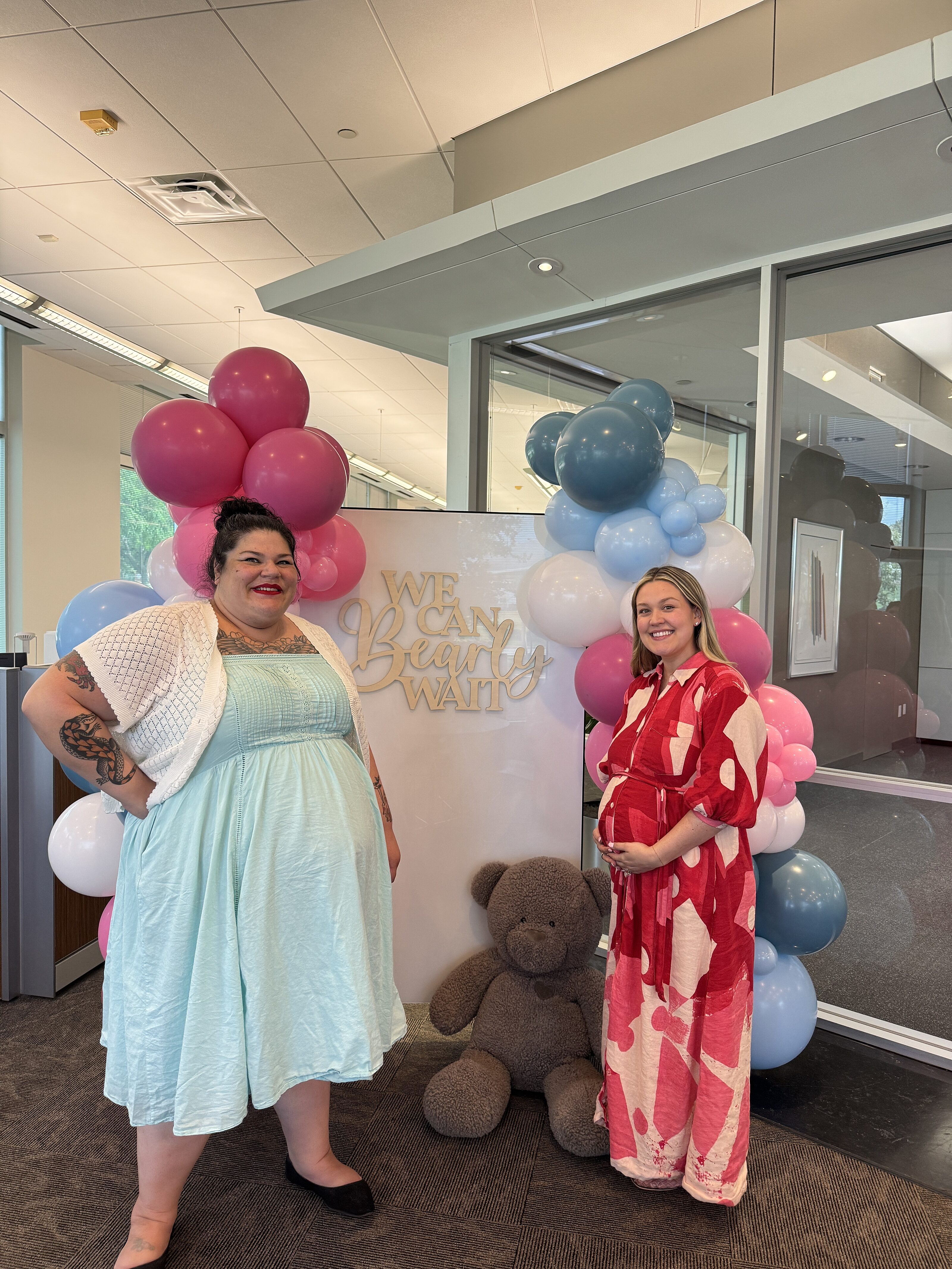 Two pregnant women smiling for a picture in front of a balloon arch at their baby shower