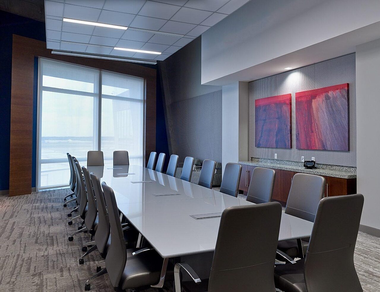 corporate office conference room with a large long rectangular white table and 20 high back grey chairs
