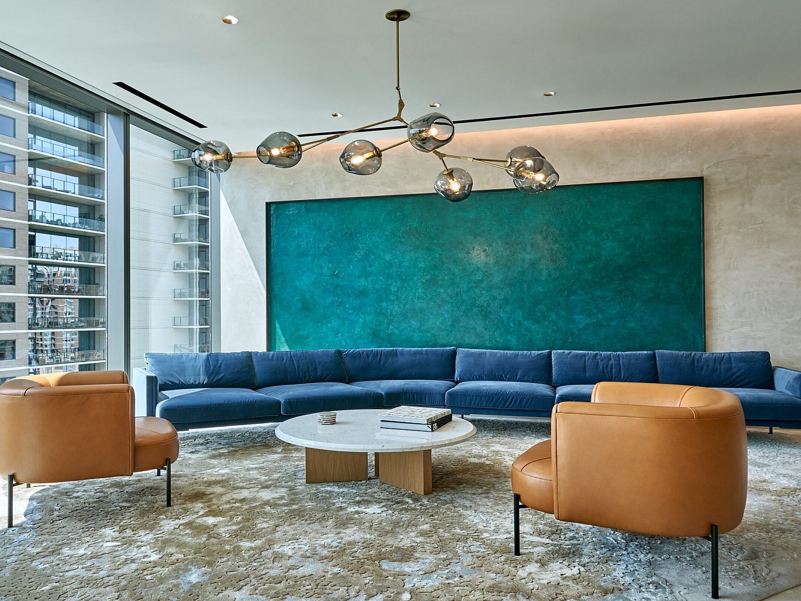 Katten seating area with a long blue sectional and two brown leather chairs surrounding a white circular coffee table