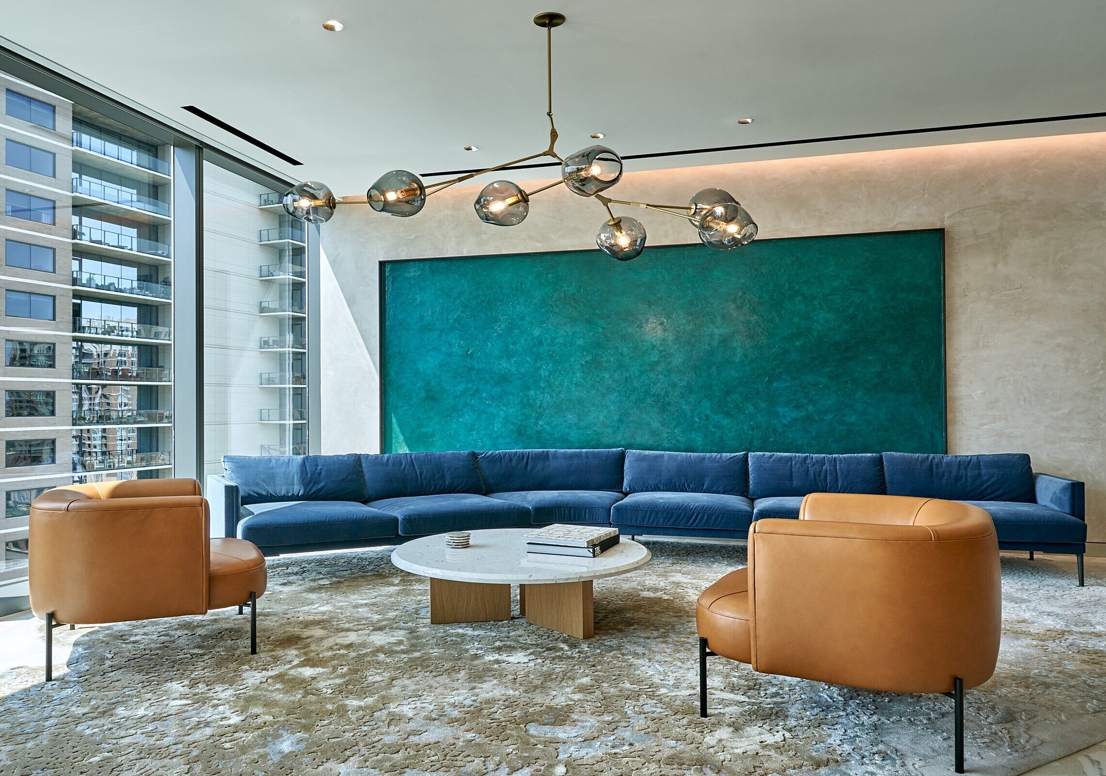 Katten seating area with a long blue sectional and two brown leather chairs surrounding a white circular coffee table