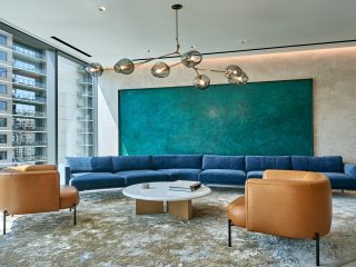 Katten seating area with a long blue sectional and two brown leather chairs surrounding a white circular coffee table