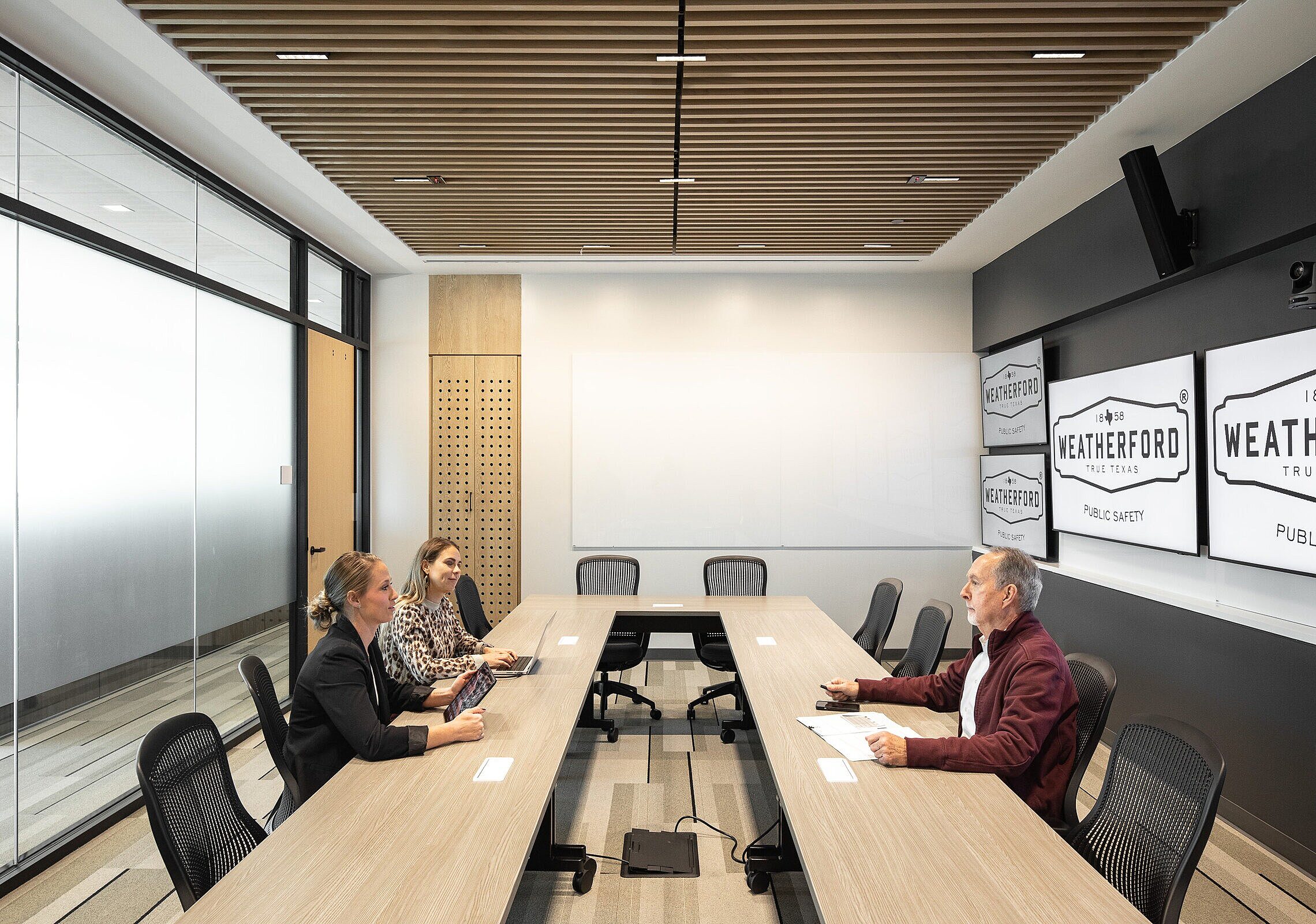 City of Weatherford Public Safety Building Meeting Room with a large rectangular wooden conference room, black ergonomic chairs, and 3 people sitting